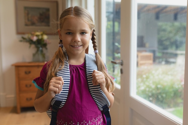 Cute girl with school bag looking at camera in a comfortable home