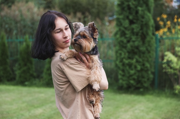 Милая девочка с йоркширским терьером на улице обнимает свою собачку в парке