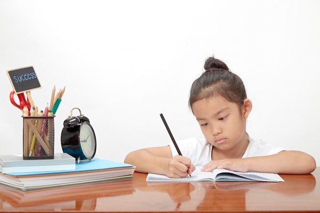 Photo cute girl writing in book on desk against white background