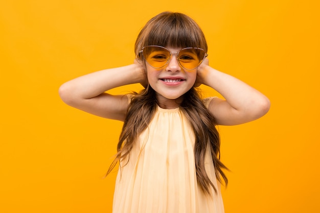노란 안경에 귀여운 소녀는 오렌지 벽에 그녀의 귀를 덮고