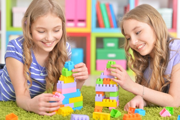 Cute girls playing together while lying on floor with green carpet