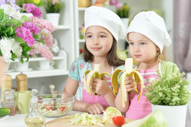 Cute girls preparing delicious fresh salad and eating bananas