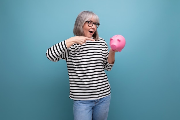 Cute grandmother old woman s holding a piggy bank with a pension on a bright background with copy