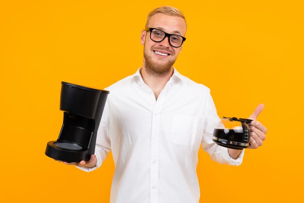 Cute guy consultant in a white shirt holds a coffee machine and a mug of coffee on yellow