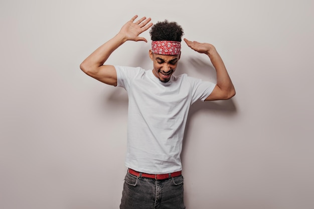 Cute guy in white Tshirt and bandana is dancing on isolated background Happy man in black pants and red headband moves and has fun