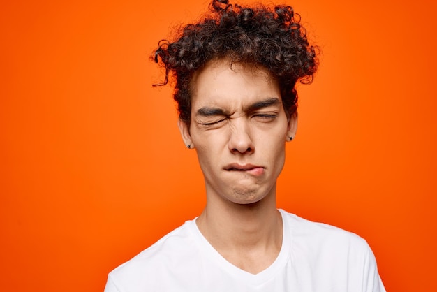 Photo cute guy in white tshirt curly hair grimace orange background high quality photo