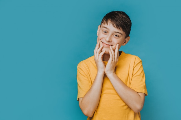 Cute handsome boy in yellow t-shirt touching his face, looking with tenderness, feels caress, happy to be healthy and have a good friends