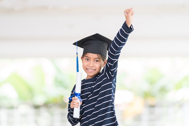 Cute happy Asian school kid graduate with graduation hat and a diploma isolated on white background