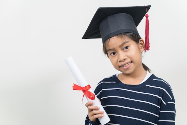 かわいい幸せなアジアの学校の子供は、卒業の帽子と白い背景で隔離の卒業証書で卒業します