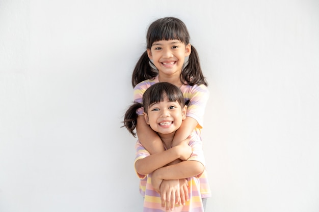 Cute happy Asian siblings hugging cuddling feeling love and connection, smiling kid girl sister embracing little girl sister on white background, 2 children good relationships