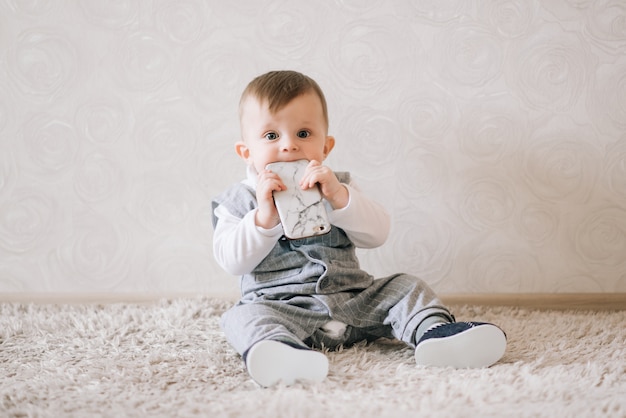 Neonato felice sveglio nel vestito alla moda del signore che si siede sul bianco