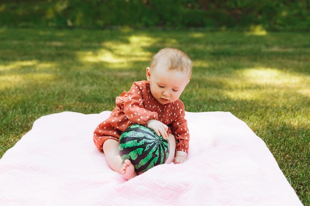 ボールを持つかわいい幸せな赤ちゃんの女の子は公園の緑の芝生の上に座っています