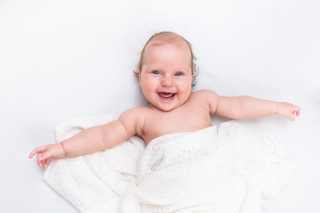 귀여운 행복한 아기는 흰색 시트에 누워 모직 천으로 덮여 있습니다