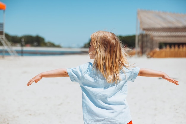 Cute happy blond boy playing on the city beach running and having fun