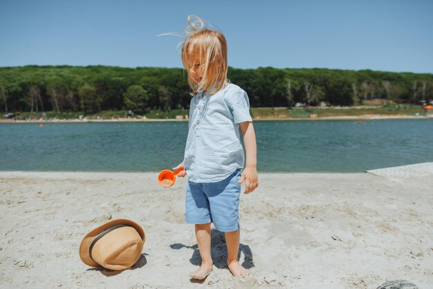 Cute happy blond boy playing with beach toys on the sandy city beach