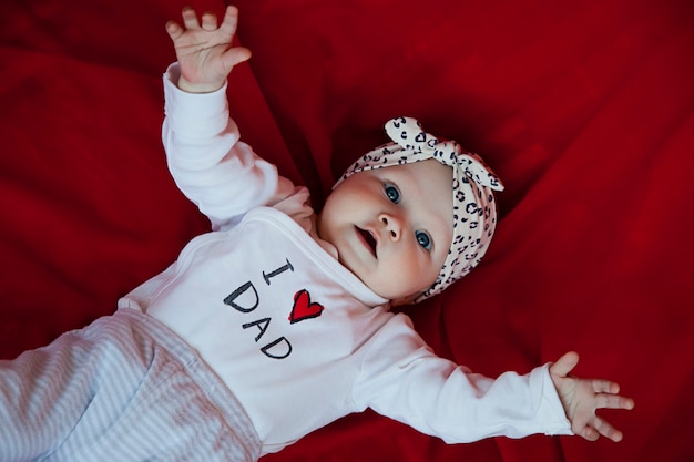 Cute happy blonde blueeyed girl three months old lying on red blanket and looking camera