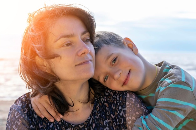 写真 かわいい幸せな男の子は、夕日の光の中で海岸に彼のお母さんを抱きしめます