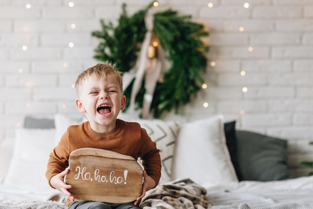 Cute happy Caucasian boy opening his presents on Christmas morning Christmas tree wreath on background Child excited and smiling Happy family holidays at home Opening gifts in boxes Copy space