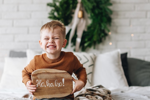 Cute happy Caucasian boy opening his presents on Christmas morning Christmas tree wreath on background Child excited and smiling Happy family holidays at home Opening gifts in boxes Copy space