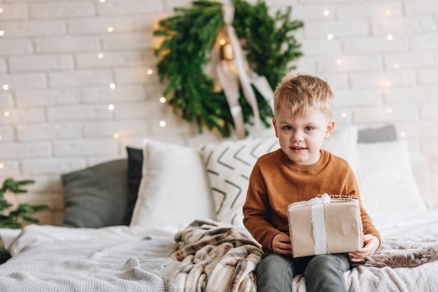 Carino felice ragazzo caucasico che apre i suoi regali la mattina di natale con lo sfondo dell'albero di natale