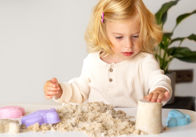 Photo cute happy caucasianblondecurlyhaired toddlerbaby girl playing with kinetic sand indoorspreschool kid early developmentmotorsensoric skills conceptcopy space