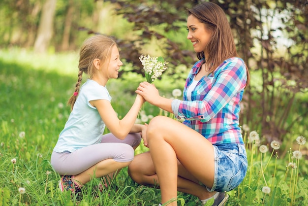 Cute happy daughter giving her smiling mom bouquet lily of the valley in the nature.