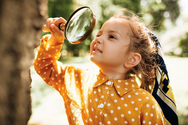 Cute happy kid with magnifying glass exploring the nature outdoor Adorable little explorer girl playing in forest with magnifying glass Curious child looking through magnifier on a sunny day in park