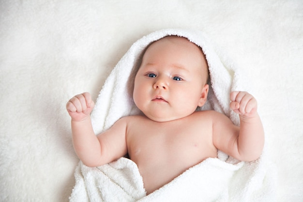 Милый счастливый маленький ребенок, спрятанный в белых полотенцах после ванны