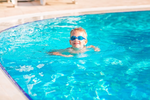 Милый счастливый маленький мальчик в очках, плавание и подводное плавание в бассейне. Плавание для детей концепции