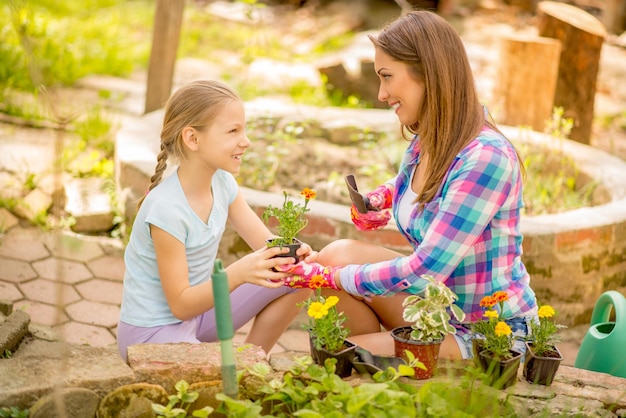 裏庭に花を植える母親を支援するかわいい幸せな少女。