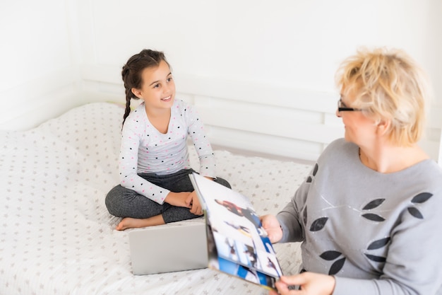 Foto bambina carina e felice che utilizza il computer portatile con sua nonna, studiando attraverso il sistema di e-learning online.