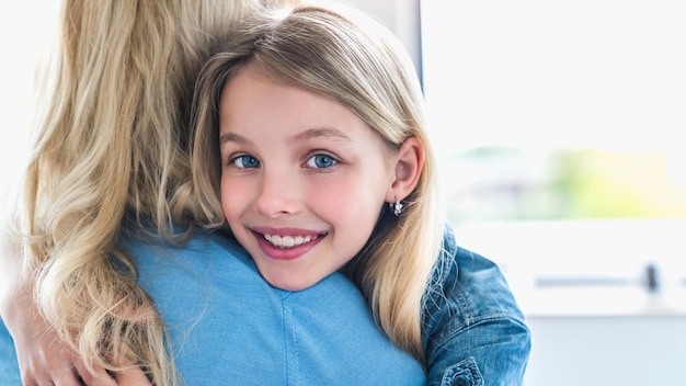 Cute happy little girl hugging her mother and looking at camera at home