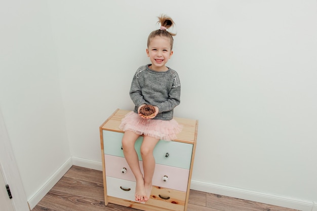 Foto bambina felice carina con acconciatura divertente con ciambella al cioccolato e bottiglia di latte sfondo bianco