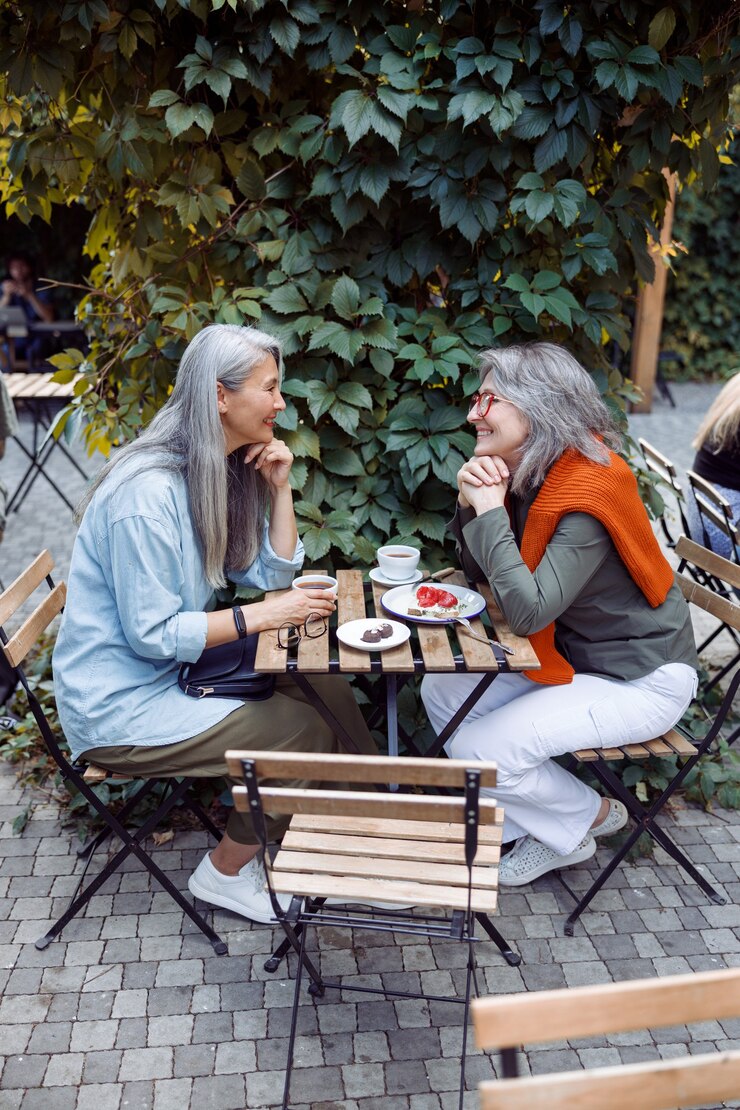 Cute happy mature women sit together on outdoors cafe terrace
