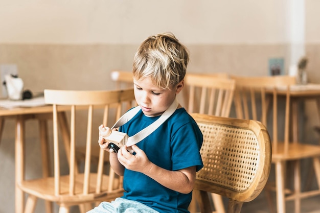 Carino sorriso felice ragazzino giocare a mano in legno macchina fotografica tenere giocattolo nelle mani attività di artigianato artistico bambini in età prescolare capacità di sviluppo futuro creativo professione moderna accogliente classe