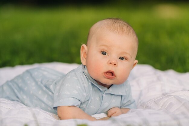 Cute happy toddler lying on a blanket on the grass outdoors in summer