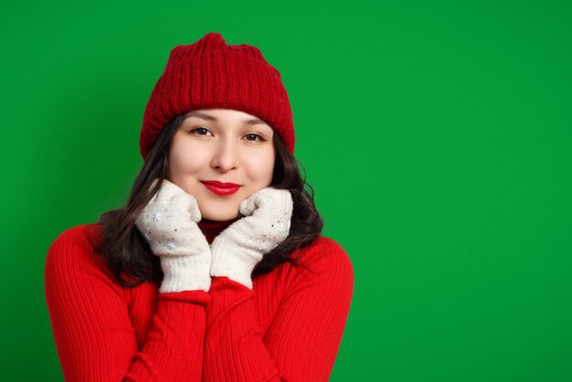 Cute happy woman in red knitted hat, sweater and mittens on green background.