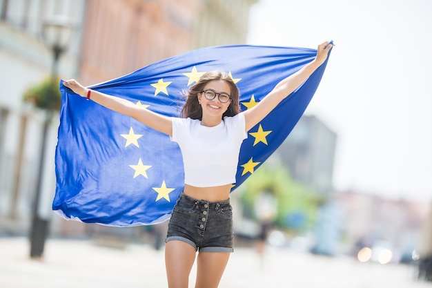 Cute happy young girl with the flag of the European Union in the streets somewhere in europe.