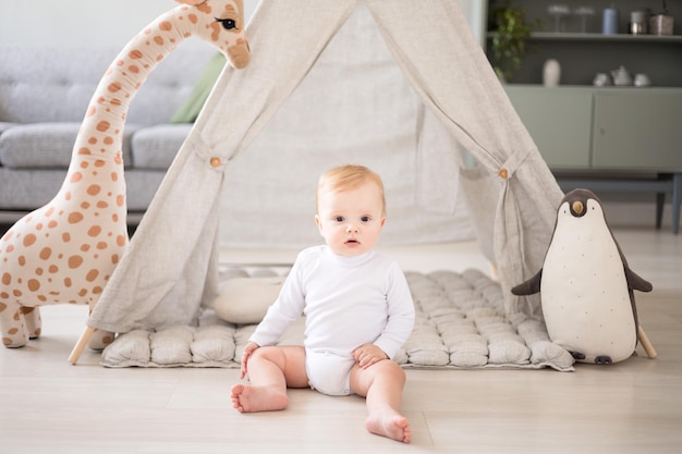 A cute healthy baby boy in a spacious bright children's room at home with a wigwam soft toys children's textiles A child is playing in the living room of the house