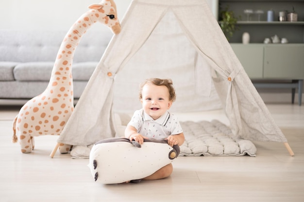 A cute healthy baby boy in a spacious bright children's room at home with a wigwam soft toys children's textiles A child is playing in the living room of the house