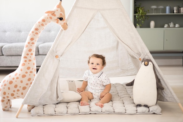 A cute healthy baby boy in a spacious bright children's room at home with a wigwam soft toys children's textiles A child is playing in the living room of the house