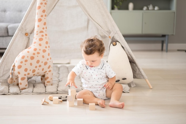 A cute healthy baby boy in a spacious bright children's room at home with a wigwam soft toys children's textiles A child is playing in the living room of the house