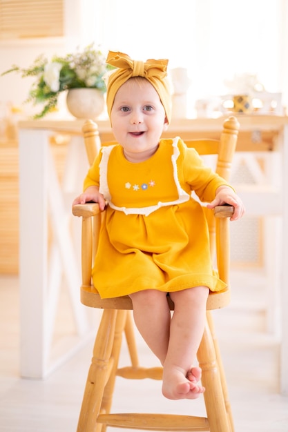노란색 면 드레스를 입은 귀여운 건강한 소녀가 집 부엌의 높은 의자에 앉아 아이들에게 이유식을 먹입니다