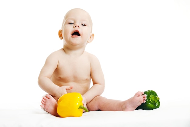 Cute healthy little girl in a pink bodysuit sitting with vegetables on a white background isolate the concept of the first lure