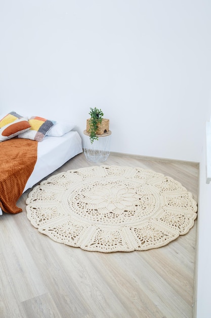 Cute homemade knitted pattern of thick threads made by hand a handmade rug made of beige threads lies in the bedroom near the bed the art of knitting