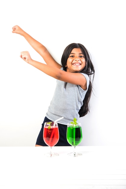 Cute Indian asian little girl posing with cold drink or fresh juice at table over white background