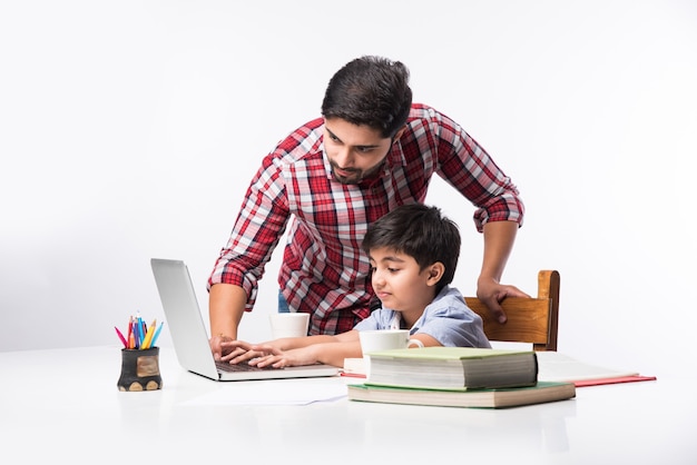 Cute Indian boy with father or male tutor doing homework at home using laptop and books - online schooling concept