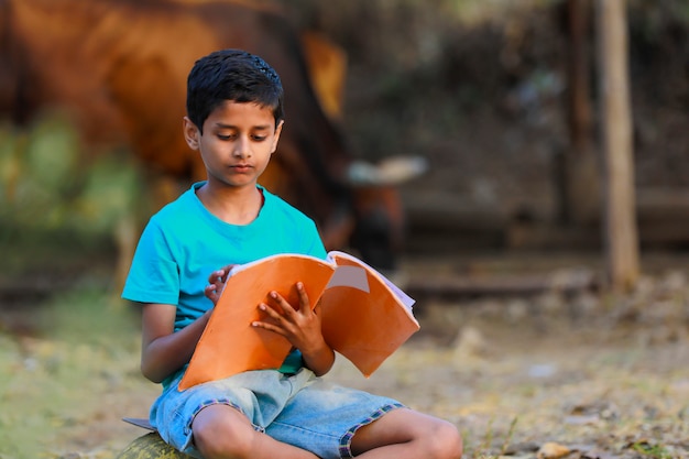 Photo cute indian child reading his book at cattle shed