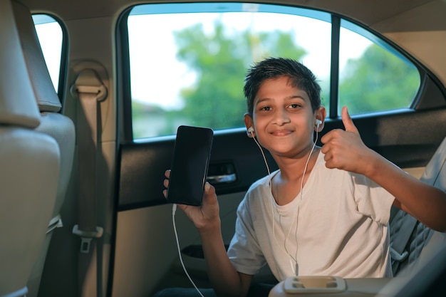 Cute indian child showing smart phone with thumps up in car window