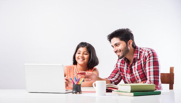 Cute Indian girl with father studying or doing homework at home using laptop and books - online schooling concept